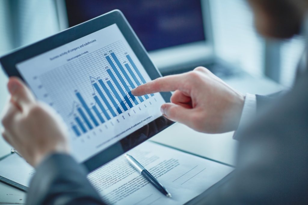 A man uses a tablet to look at a graph showing fluctuating figures trending upward.