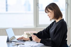 A woman using a laptop with a calculator and documents.