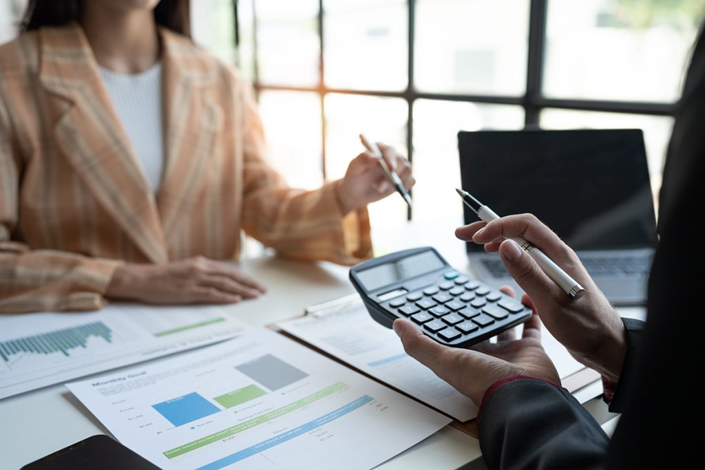 Two professionals in an office with one person holding a calculator.
