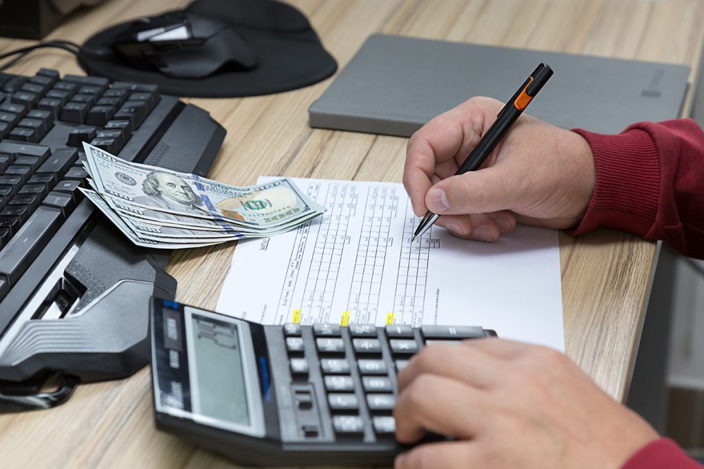 A professional making some calculations on a calculator with some hundred dollar bills sitting nearby